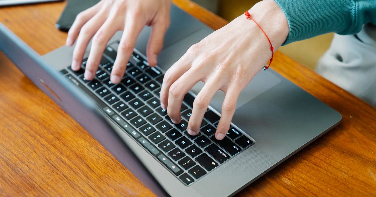 Hands typing on a laptop keyboard on a wooden table